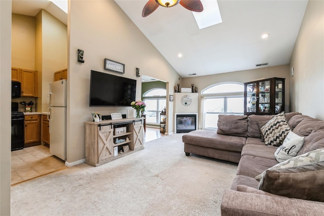 living area with visible vents, light carpet, a skylight, high vaulted ceiling, and ceiling fan