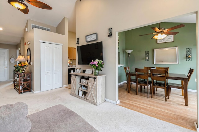 living area with light colored carpet, baseboards, a ceiling fan, and high vaulted ceiling