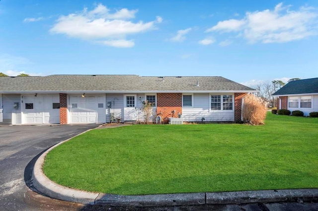 ranch-style house featuring driveway, an attached garage, a front yard, brick siding, and roof with shingles