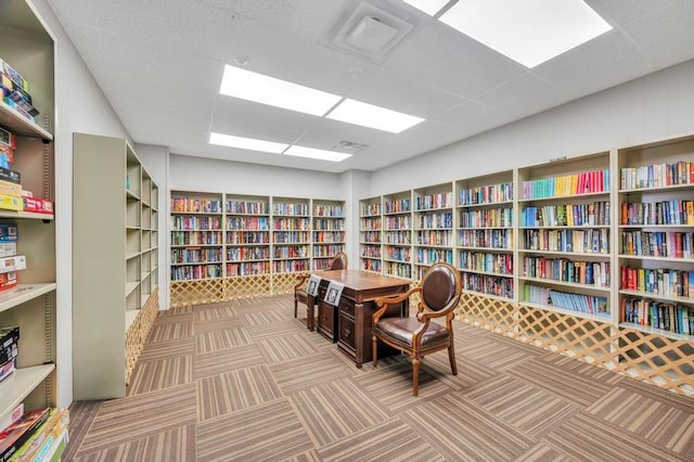 sitting room with wall of books, a paneled ceiling, and carpet