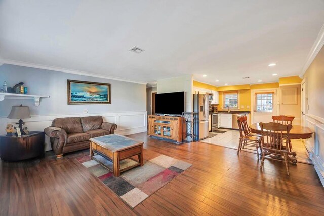 living area with light wood-style flooring, a wainscoted wall, and ornamental molding