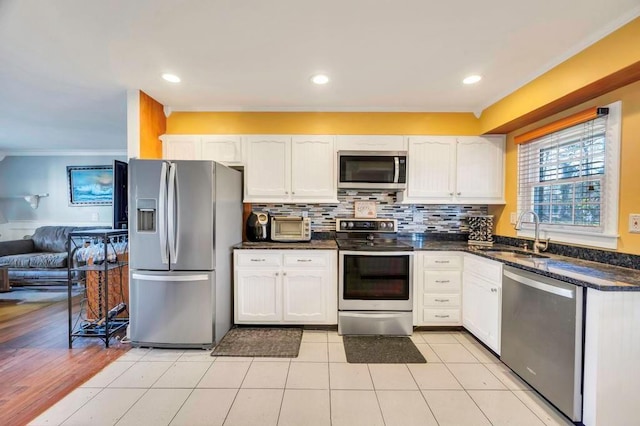 kitchen featuring ornamental molding, a sink, tasteful backsplash, appliances with stainless steel finishes, and white cabinetry