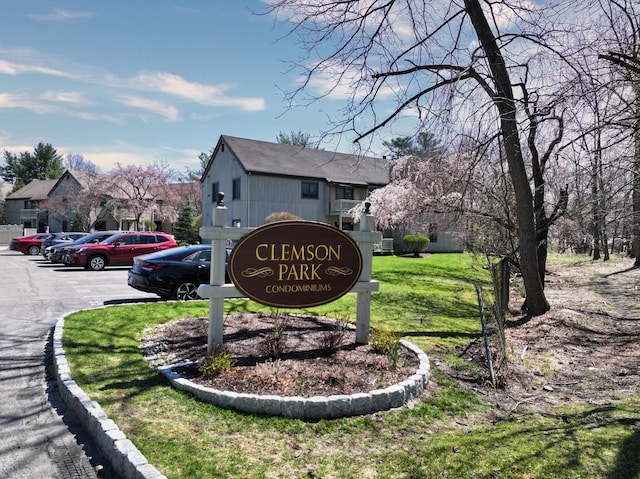 community / neighborhood sign featuring a lawn and uncovered parking