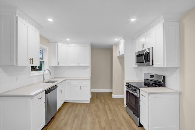 kitchen with baseboards, white cabinetry, appliances with stainless steel finishes, light wood finished floors, and a sink