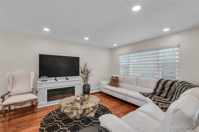 living room featuring a baseboard heating unit, recessed lighting, wood finished floors, and a glass covered fireplace