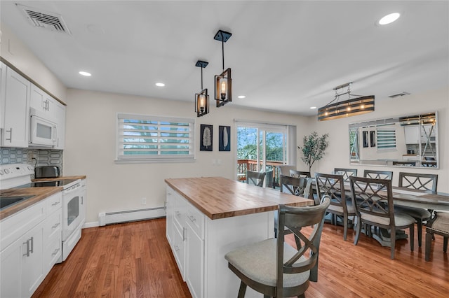 kitchen featuring white appliances, butcher block countertops, a baseboard radiator, a breakfast bar, and visible vents