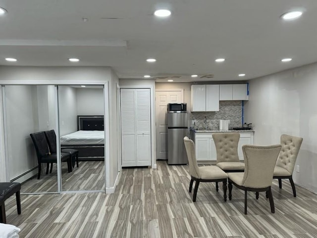 kitchen with appliances with stainless steel finishes, white cabinetry, light wood-type flooring, and backsplash