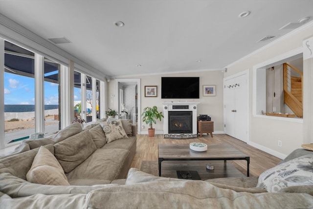living area with baseboards, crown molding, a glass covered fireplace, and wood finished floors