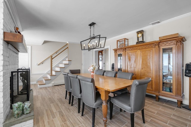 dining area featuring light wood finished floors, an inviting chandelier, visible vents, a fireplace, and stairs