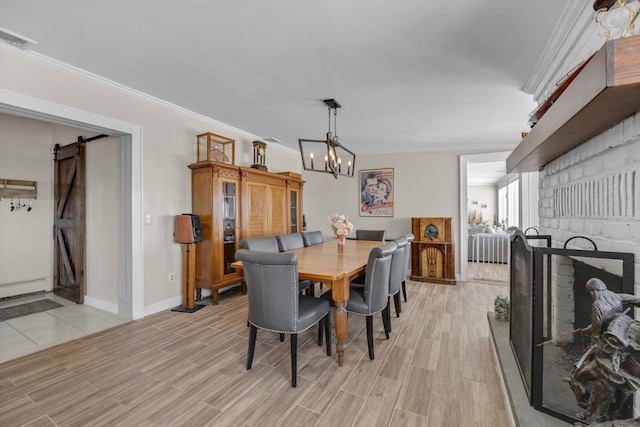 dining space featuring a chandelier, light wood finished floors, crown molding, and a barn door