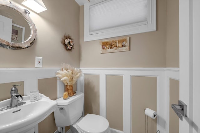 half bath with wainscoting, toilet, a sink, and a decorative wall