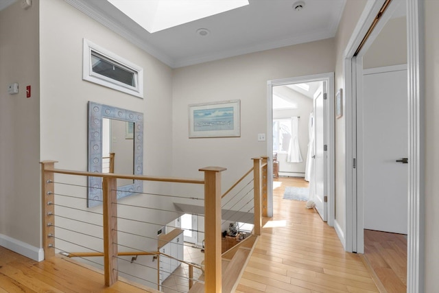 corridor with light wood-type flooring, an upstairs landing, a skylight, baseboard heating, and ornamental molding