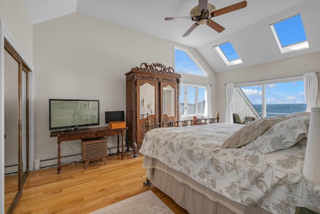 bedroom with ceiling fan, lofted ceiling with skylight, baseboard heating, and wood finished floors
