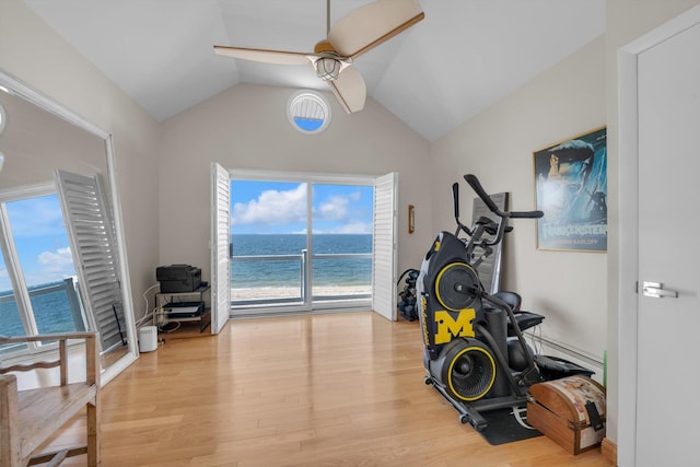 workout area with a ceiling fan, wood finished floors, a water view, and vaulted ceiling