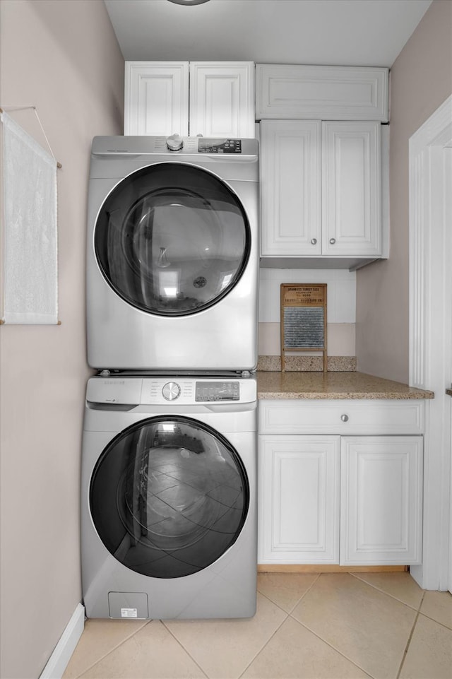laundry area with stacked washer and clothes dryer, baseboards, cabinet space, and light tile patterned floors