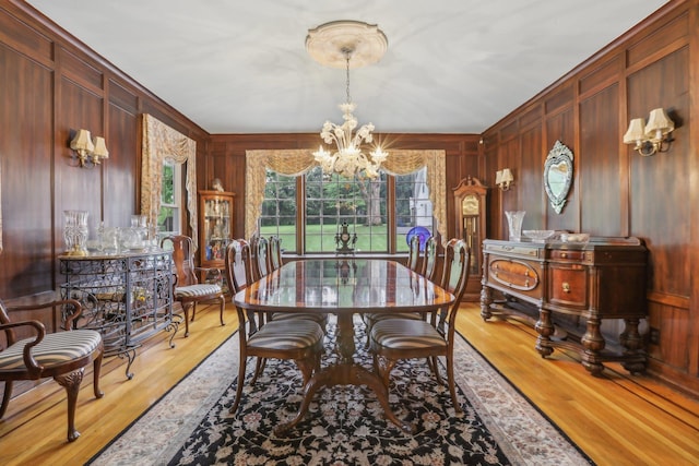 dining space with light wood finished floors, a notable chandelier, and wooden walls