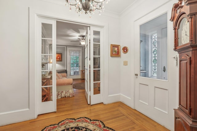 entrance foyer with light wood-style flooring, french doors, ceiling fan with notable chandelier, baseboards, and ornamental molding