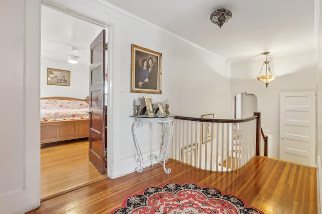 corridor with crown molding, arched walkways, wood finished floors, and an upstairs landing