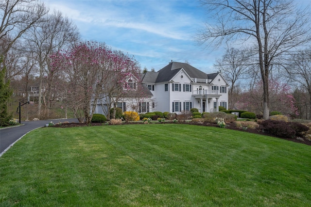 view of front of home with aphalt driveway, a balcony, and a front yard