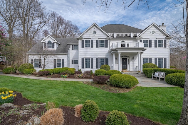 view of front of property featuring a chimney, a front lawn, roof with shingles, and a balcony