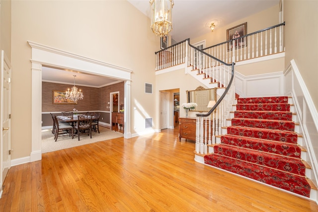 entrance foyer with a towering ceiling, visible vents, an inviting chandelier, wood finished floors, and stairs
