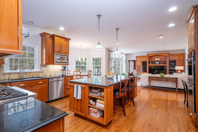 kitchen featuring light wood finished floors, a kitchen breakfast bar, a sink, open floor plan, and appliances with stainless steel finishes