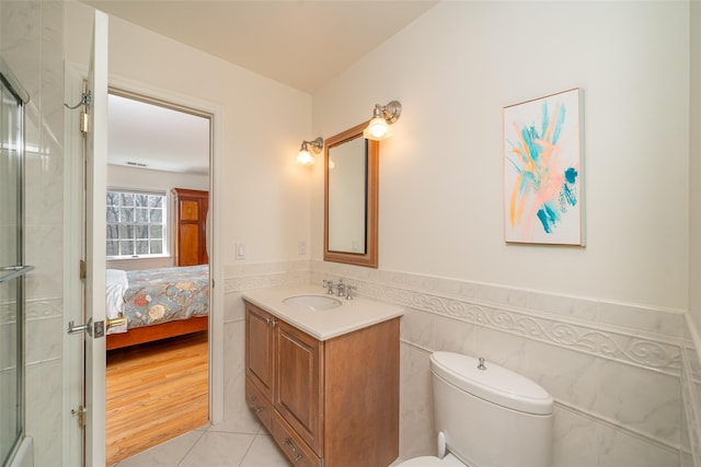 ensuite bathroom with a shower with door, toilet, vanity, wainscoting, and ensuite bathroom
