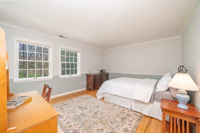 bedroom with visible vents, baseboards, light wood-style floors, and ornamental molding