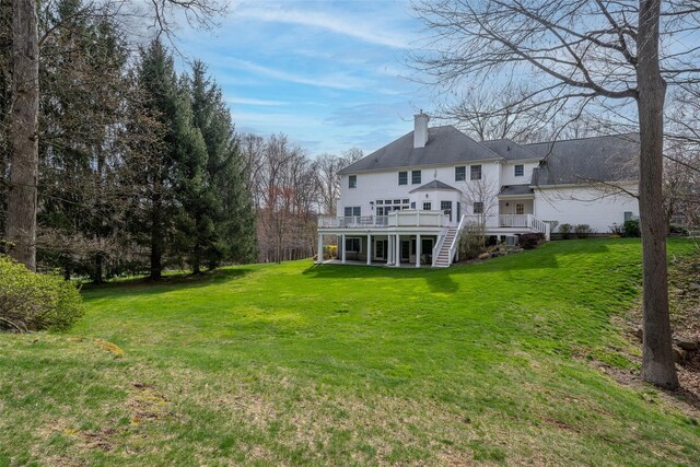 back of property with a chimney, a wooden deck, stairs, and a lawn