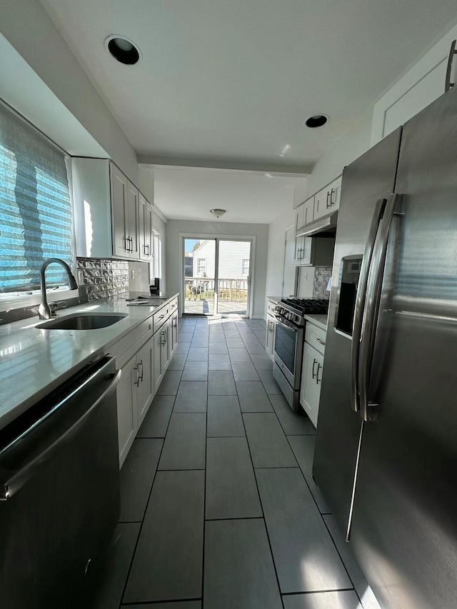 kitchen with white cabinets, light countertops, a sink, stainless steel appliances, and backsplash
