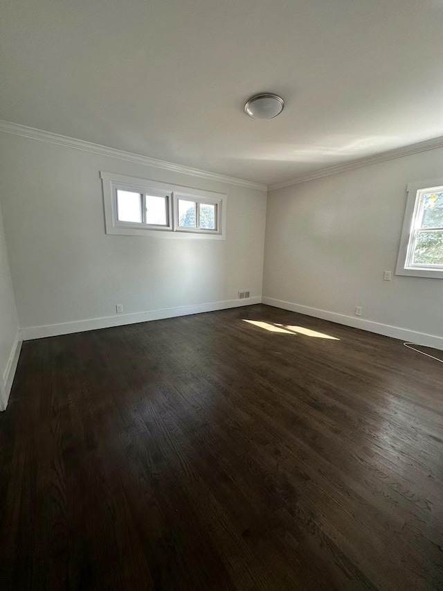 spare room featuring crown molding, baseboards, and dark wood finished floors