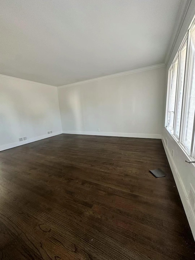spare room featuring visible vents, baseboards, ornamental molding, and dark wood-style floors