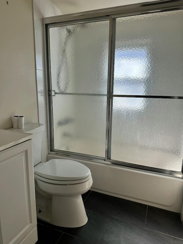 bathroom with toilet, tile patterned floors, combined bath / shower with glass door, and vanity