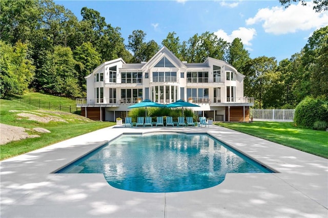 rear view of property with a patio area, a balcony, a lawn, an outdoor pool, and fence