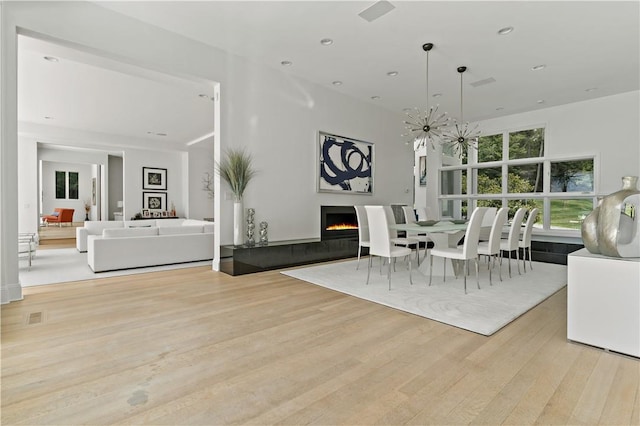 dining space featuring visible vents, wood finished floors, a warm lit fireplace, and recessed lighting