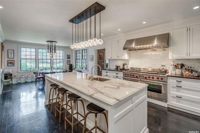 kitchen featuring white cabinets, designer stove, wall chimney exhaust hood, and a sink