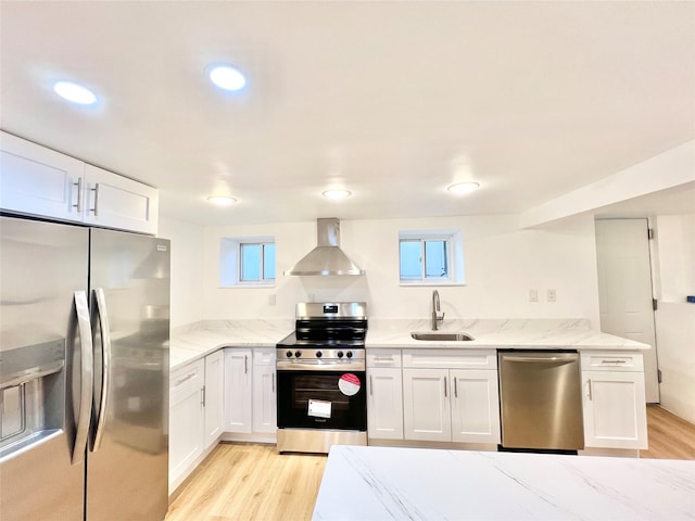 kitchen with white cabinets, stainless steel appliances, wall chimney range hood, a sink, and light wood-style flooring