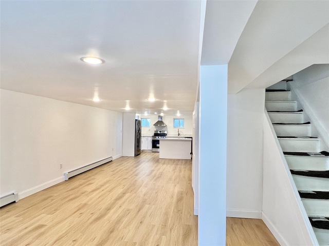 finished below grade area with a baseboard radiator, baseboards, light wood finished floors, and freestanding refrigerator