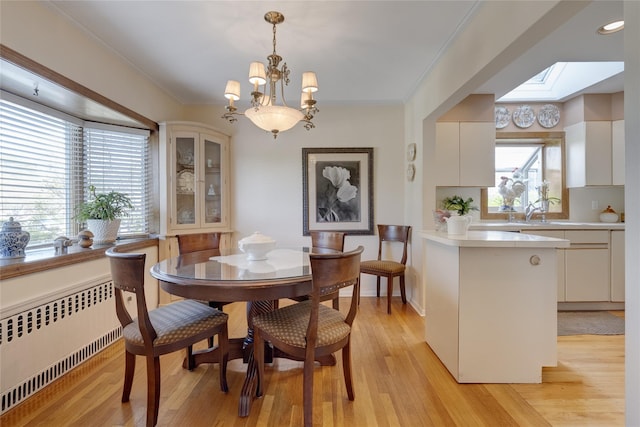 dining room with radiator, a skylight, healthy amount of natural light, ornamental molding, and light wood-style floors