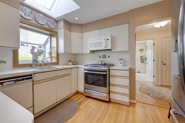 kitchen featuring stainless steel appliances, a skylight, light countertops, a sink, and light wood-style floors