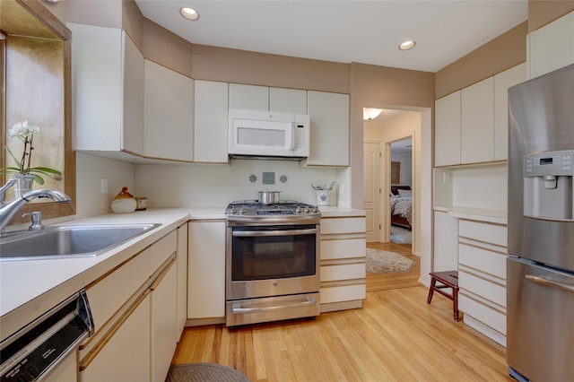 kitchen with stainless steel appliances, a sink, light countertops, light wood-style flooring, and recessed lighting