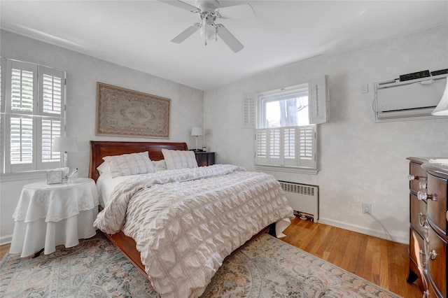 bedroom with radiator heating unit, wood finished floors, baseboards, a ceiling fan, and a wall mounted air conditioner