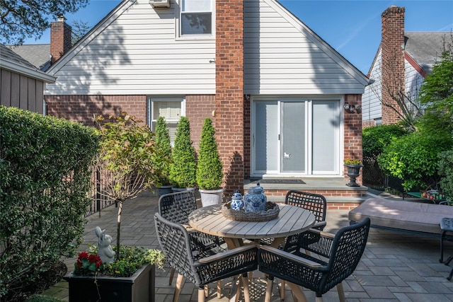 rear view of house with brick siding, a patio, and outdoor dining area