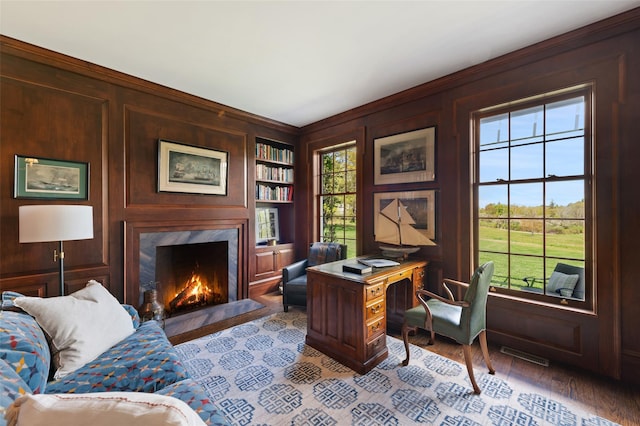 office with visible vents, wood walls, wood finished floors, a fireplace, and built in shelves