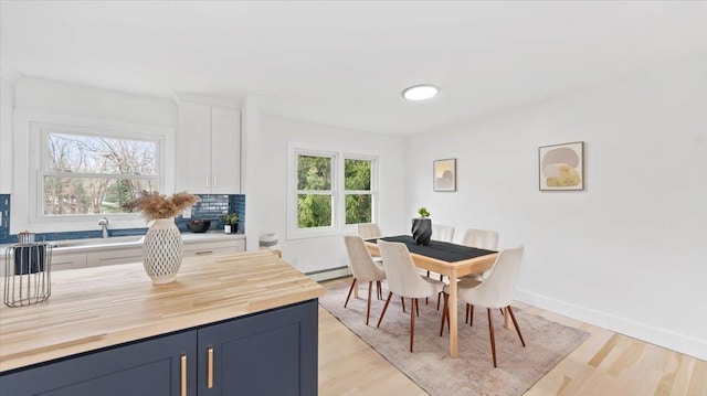 dining area featuring light wood-type flooring, baseboard heating, and baseboards