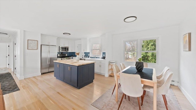 kitchen with white cabinets, plenty of natural light, light wood-style floors, appliances with stainless steel finishes, and baseboard heating