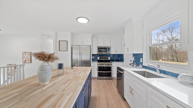 kitchen featuring backsplash, a sink, butcher block counters, appliances with stainless steel finishes, and white cabinetry