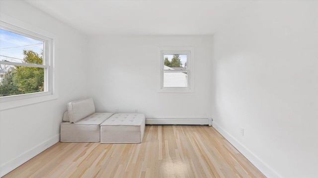 unfurnished room with a baseboard heating unit, wood finished floors, and baseboards