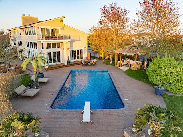 pool with a diving board, a gazebo, an outdoor hangout area, and a patio area