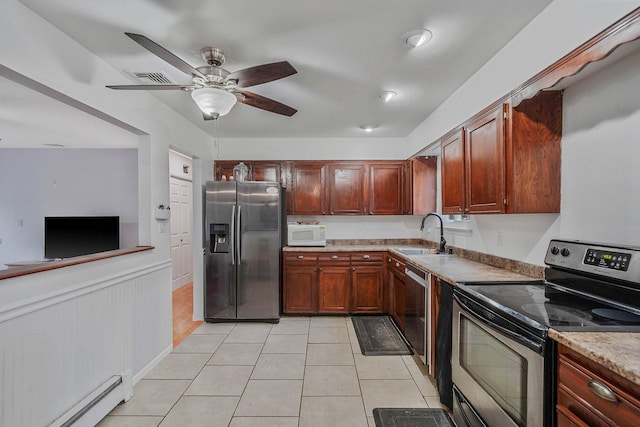 kitchen with a ceiling fan, light tile patterned floors, a baseboard heating unit, a sink, and appliances with stainless steel finishes